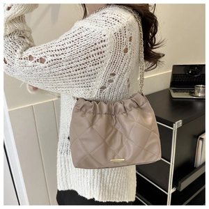 Detail of quilted beige crossbody bag with chain strap shown on a model in office