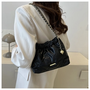 Detail showing black quilted chain shoulder bag texture with golden metal trim on white suit