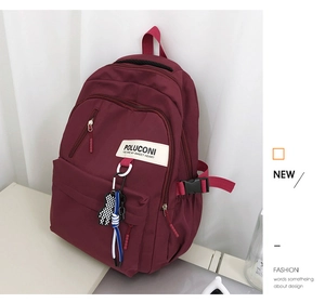 Vue détaillée du sac à dos bordeaux en nylon imperméable avec pendentif ours et boucle latérale