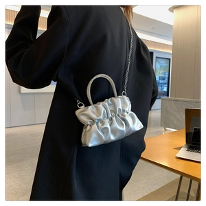 Detail of silver pleated crossbody bag with sparkling rhinestone handle on black blazer