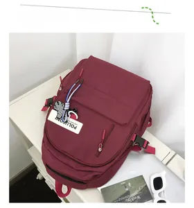 Détail du sac à dos en toile bordeaux montrant la boucle latérale et la poche avant zippée