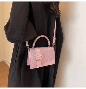 Sac à main rose pailleté porté sur un manteau noir avec bandoulière et poignée