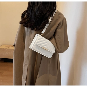 White quilted crossbody bag with gold hardware shown on model in brown coat