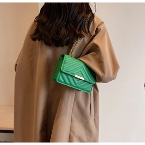 Detail view of green leather crossbody bag with V-quilt pattern and gold chain strap