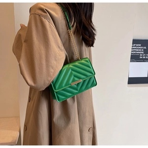Detail of green chevron quilted crossbody bag with gold chain strap worn with trench coat