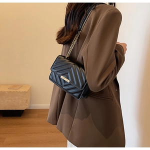 Detail view of a black quilted crossbody bag with gold chain and metal clasp