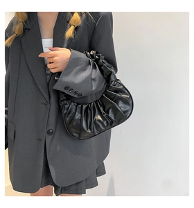 Close-up of a black pleated crescent handbag featuring soft cloud-like ruffles and texture