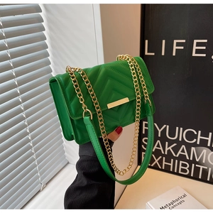 Detailed view of a green quilted crossbody bag with a gold chain strap held by hand