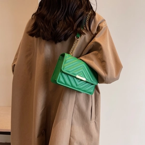 Green quilted faux leather crossbody bag with gold chain strap on a trench coat model