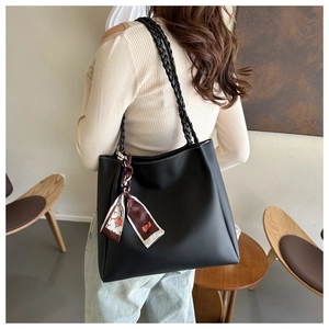 Detail view of black leather tote bag with woven shoulder strap and decorative silk scarf