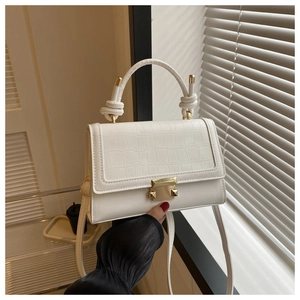 Detail of white crocodile pattern handbag with metal buckle and knot handle in natural light