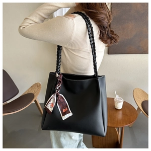 Close-up of black leather tote bag with woven handles and decorative printed silk scarf