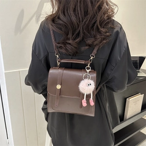 Mini brown faux leather backpack worn by model featuring a pink plush monster charm