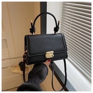Detail of black crossbody bag with crocodile pattern and golden metal lock mechanism