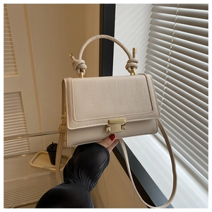 Close-up of cream PU leather handbag featuring faux crocodile texture and knot handle design