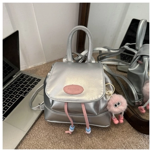 Close-up of silver PU leather backpack with pink logo patch and plush monster charm