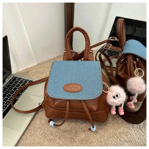 Detail of a mini backpack with brown faux leather, denim flap, and a plush monster charm