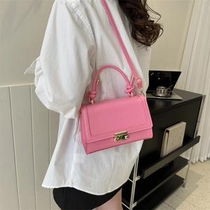 Pink crocodile-embossed small square bag with gold metal lock being worn by a model