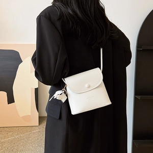Minimalistische weiße Leder-Umhängetasche mit Elefanten-Anhänger an Modell im Innenraum