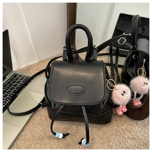Detail of a black mini leather backpack with drawstring closure and a plush pink charm