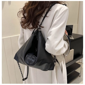 Détail du logo circulaire en relief et de la bandoulière en chaîne sur un sac fourre-tout noir