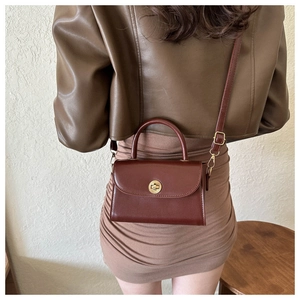 Close-up of vintage burgundy crossbody bag with gold round clasp and leather texture