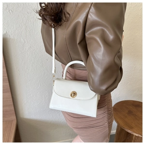 Detail of white PU leather crossbody bag featuring a round golden twist-lock closure