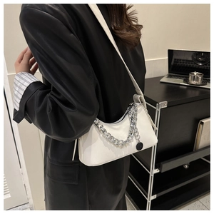 Close-up of minimalist white leather underarm bag with silver chain and black pendant