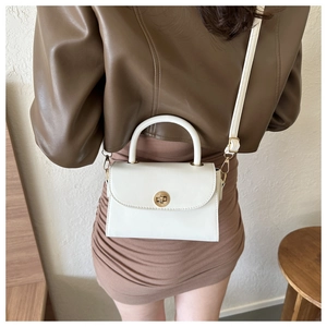 Detail of white mini square bag with golden twist lock worn with a leather jacket