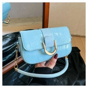 Close-up of light blue crocodile embossed handbag with golden U-shaped buckle and metal chain
