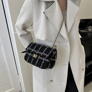 Petit sac bandoulière en tweed noir et bleu avec chaîne dorée sur un trench-coat beige