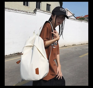 Detail of white nylon backpack featuring brown leather DAY logo patch and zipper pull