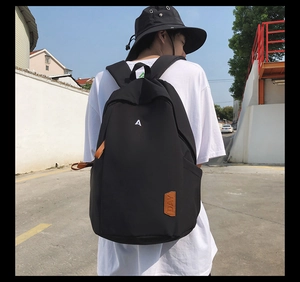Detail of black backpack with white letter A embroidery and brown leather label