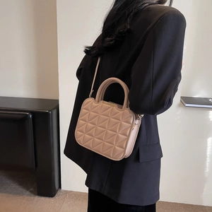 Beige quilted shoulder bag with gold metal trim and round handle on a black blazer