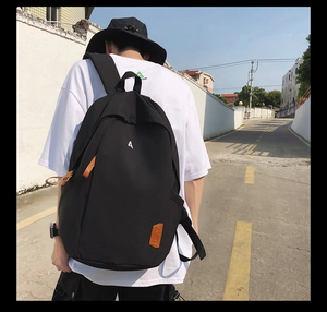 Detail of minimalist black backpack featuring white embroidered A and brown leather patch