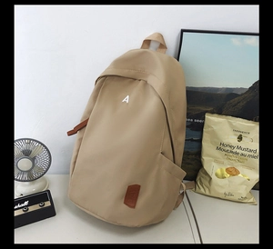Detail view of khaki nylon backpack with white letter A print and brown leather brand patch