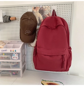 Detailaufnahme eines weinroten Rucksacks mit gewebtem Reißverschlussanhänger an Lochwand