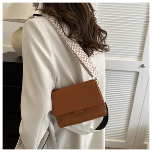 Detail view of brown leather square crossbody bag with stylish wide geometric patterned strap