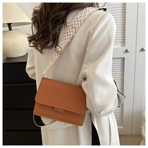 Brown crossbody bag with patterned wide strap worn over a white blazer for autumn