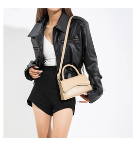 Detail of minimalist beige square crossbody bag styled with a leather jacket on model