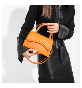 Close-up of bright orange glossy leather square bag with metallic zipper and curved flap