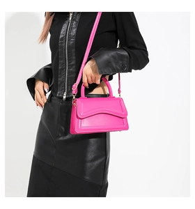 Detail of a structured hot pink crossbody bag with gold hardware and smooth faux leather