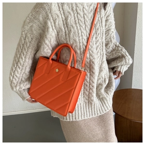 Detail of orange quilted handbag with a golden floral emblem and slim shoulder strap