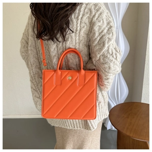 Detail of a bright orange quilted tote bag with golden flower hardware and long strap