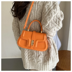 Détail du sac à main en cuir orange avec boucle dorée et bandoulière sur un modèle