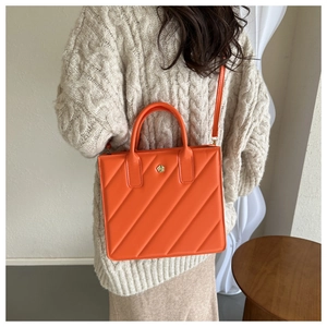 Detail of orange quilted handbag featuring a golden flower clasp and leather texture