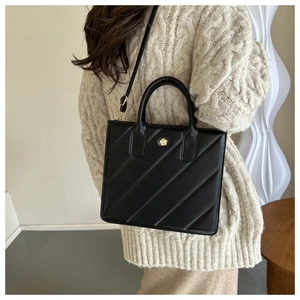 Detail of black quilted leather handbag with gold flower clasp shown on model