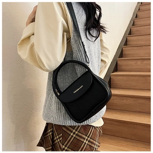 Black leather small square bag shown as a crossbody purse on a model in a natural setting