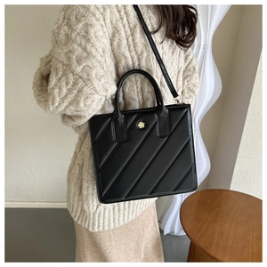 Detail of black quilted tote bag featuring a golden camellia flower metal ornament
