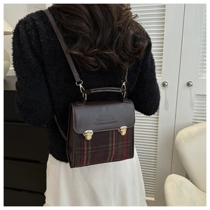 Detail of vintage plaid backpack showing leather flap with gold metal buckles on a model